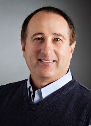 A smiling middle-aged man wearing a navy sweater over a light blue shirt. This portrait conveys approachability and professionalism.